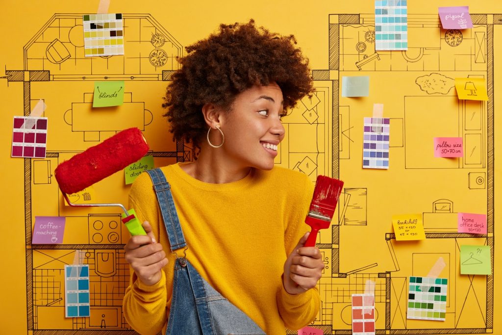 African American female decorator holds paint brush and roller